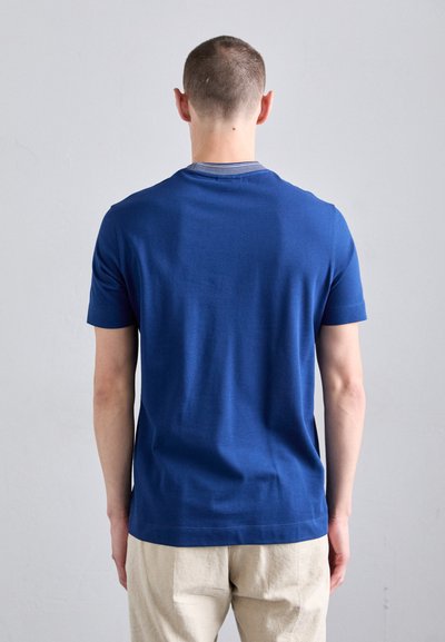 T-shirt bleu marine à manches courtes avec col rond et une texture lisse, associé à un pantalon beige clair. Design minimaliste sans ornements.
