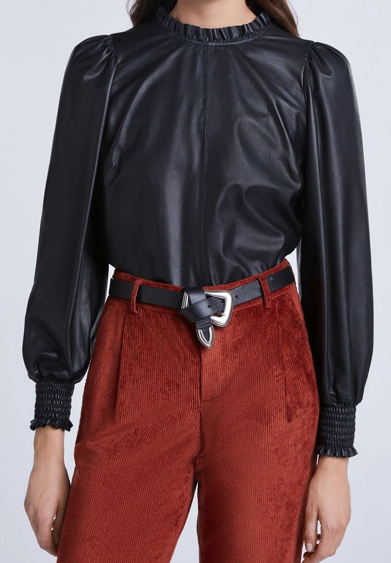 Svart läderblus med puffärmar och volangkrage; kombinerad med rödbruna kordbyxor med texturerad yta och bälte i midjan.