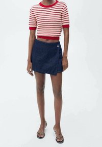 Gestreepte rood-witte gebreide trui met korte mouwen, gecombineerd met een donkere denim A-lijn wikkelrok, voorzien van knoopaccenten en een gladde textuur.