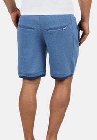 Shorts bleu en maillot avec une finition texturée, taille élastique et ourlets de couleur marine. Comprend deux poches arrière et un logo sur le côté droit.
