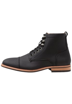 Bottine en cuir noir avec lacets sur le devant, œillets métalliques et talon empilé marron, vue de côté extérieur sur fond blanc.