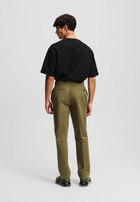 Camicia nera a maniche corte con una vestibilità morbida, abbinata a pantaloni tagliati verde oliva, entrambi con linee pulite e dettagli minimi.