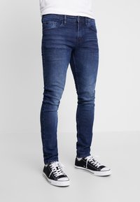 Mörkblå skinnyjeans med blekta detaljer, i bomullsmaterial, fem-fickorsdesign, kombinerat med svarta canvas sneakers med vita snören.