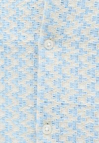 Tuvplāns zilas un baltas pundurkājaines raksta trikotāžas audumam ar divām baltām pogām, kuras ir piemeklētas pie apģērba daļas.