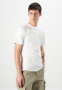 T-shirt branca de algodão com gola redonda, mangas curtas e um pequeno gráfico no peito esquerdo com chamas laranja.