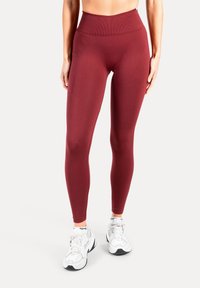 Leggings bordeaux taille haute avec un tissu lisse et extensible et un détail de poche latérale, associés à des chaussures de sport blanches.