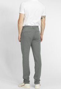 Pantalon gris en tissu tricoté texturé, avec une coupe cintrée, poches latérales, empiècement arrière et deux poches arrière.