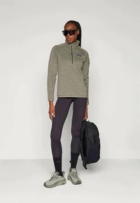 Fleece quarter-zip genser i olivengrønn, kombinert med svarte leggings og grå vandresko. Svart ryggsekk og solbriller brukt.