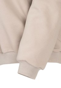 Beżowa bluzka z rękawami z ribbowanymi mankietami i miękkim, teksturowanym materiałem. Projekt obejmuje luźny krój i minimalistyczny styl.