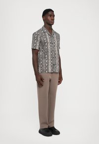 Chemise à manches courtes avec un motif serpent métallisé en gris et noir, assortie à un pantalon beige ample et des baskets noires.