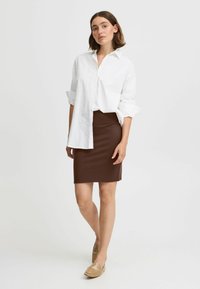 Chemise blanche à manches retroussées associée à une jupe ajustée marron et des chaussures marron clair à enfiler. Design simple et textures lisses.
