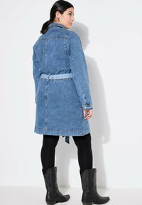 Vestido camisero de mezclilla en azul claro con mangas largas, cinturilla ajustada y detalles de botones. Combinado con leggings negros y botas de cowboy.