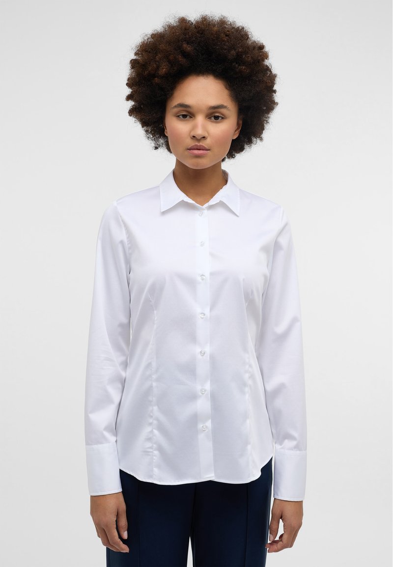 White long-sleeve shirt with a pointed collar, front button closure, and a smooth, polished texture. Features tailored fit and slight curved hem.
