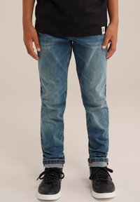 Blå denimjeans med en blekt design, slim fit, uppvikta mudd och en mjuk textur, i kombination med svarta träningsskor.