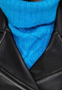 Sininen neulepusero, jossa on kaulus ja ribbitekstuuri, kerroksittain mustan nahkatakin alla. Takissa on viisto vetoketju ja sileä pinta.