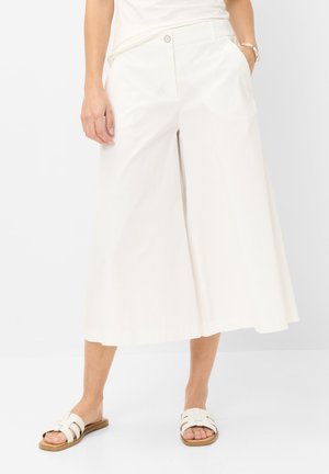 Kvinde iført hvide culottes med højtaljede, brede ben og lommer, kombineret med hvide slip-on sandaler og en hvid top.