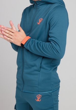 Turkusowa bluza z kapturem na zamek błyskawiczny z pomarańczowym logo i dodatkiem na nadgarstku; miękka, gładka faktura z dopasowanym krojem. Do kompletu dopasowane spodnie.