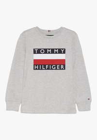 Graues Langarmshirt aus Baumwolle; mit einem schwarzen Rechteck, das den Text "TOMMY HILFIGER" sowie horizontale Streifen in Rot, Weiß und Blau zeigt.