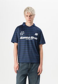 Marineblå stripete polo shirt med en brettet krage, med hvit tekst og små stjernediagrammer. Laget av et lett materiale.