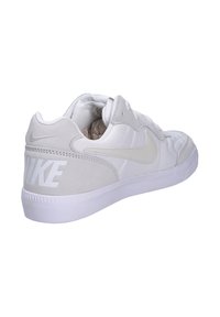 Zapatilla Nike blanca que cuenta con una parte superior de malla texturizada, acentos de ante y una suela de goma blanca. Notable logo "NIKE" en blanco en el talón.