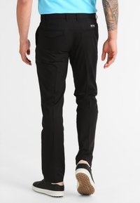 Svarta byxor med slim fit, med två bakfickor. Bärs med en ljusblå skjorta och svarta sneakers med vit sula.