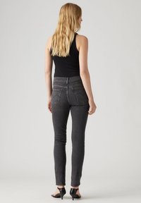 Pantalones vaqueros negros ajustados con cintura alta, piernas rectas, bolsillos traseros y una sutil textura desteñida, combinados con sandalias negras de tacón.