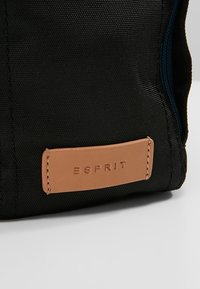 Borsa di stoffa nera con un'etichetta in pelle beige con la scritta "ESPRIT" in rilievo. Materiale testurizzato con cuciture visibili e dettaglio con cerniera.