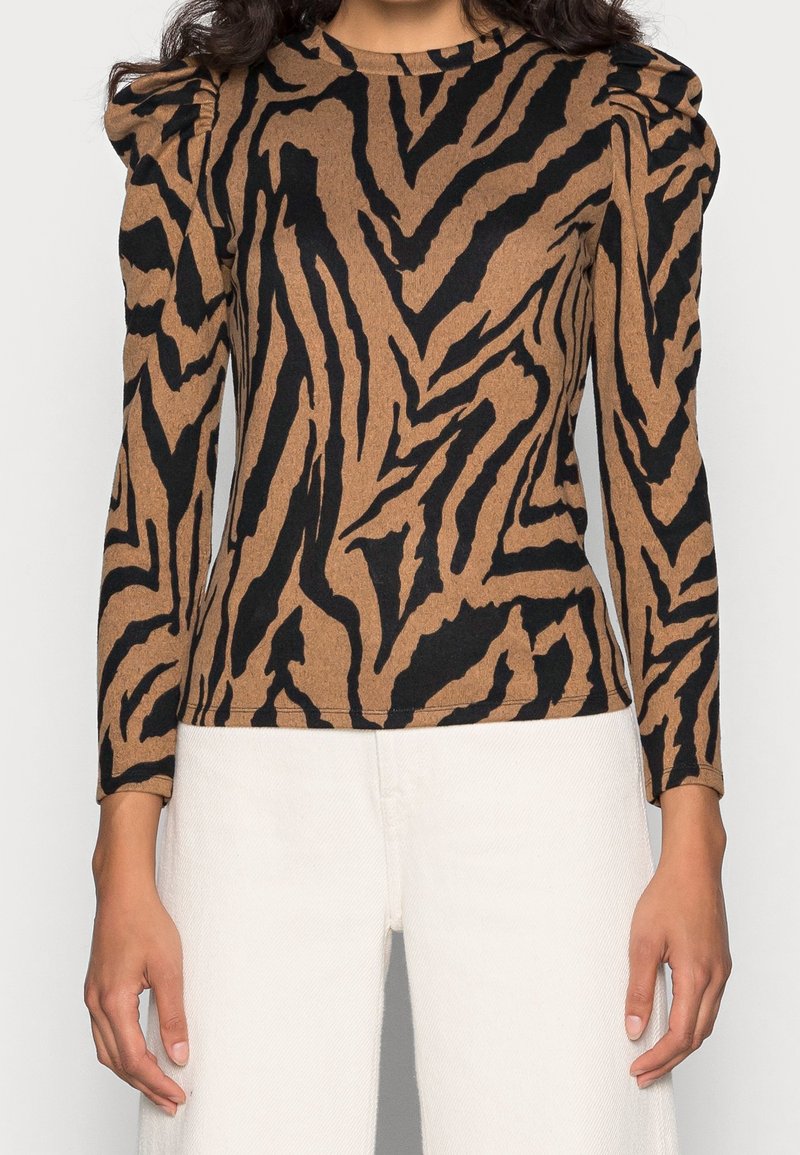 Top a maniche lunghe marrone con stampa zebra nera, caratterizzato da spalle imbottite e una texture a costine. Abbinalo a pantaloni bianchi a gamba larga.