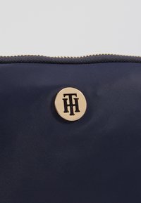 Bustina in nylon blu con logo circolare dorato e chiusura con zip. Texture liscia, con un accento di marca prominente sulla parte anteriore.