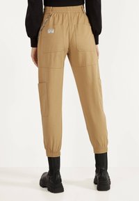 Khaki cargobroek met een elastische tailleband, voorzien van twee zijzakken en een achterzak, en afgewerkt met elastische boorden.