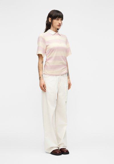 Μπλουζάκι πόλο με κοντά μανίκια και ρίγες σε ροζ και κρεμ χρώμα, με γιακά και κουμπιά μπροστά. Συνδυασμένο με άνετο, λευκό παντελόνι και καφέ παπούτσια.