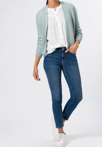 Světle modrý pletený cardigan přes bílou košili s knoflíky, doplněný o tmavě modré skinny džíny a bílé tenisky.