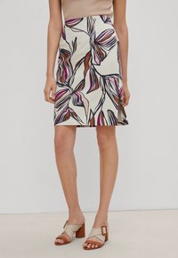 Une jupe mi-longue présentant un imprimé floral dans des tons de brun, rose et violet sur un fond crème, confectionnée dans un tissu lisse.