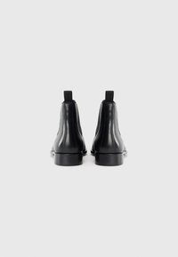 Botas de tobillo de cuero negro con textura suave, paneles laterales elásticos y lengüetas de tiro. Diseño minimalista icónico y forma de punta redonda.