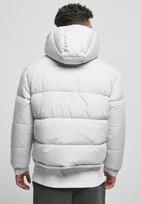 Hellgraue Pufferjacke mit Kapuze, ausgestattet mit einem gesteppten Design, elastischen Bündchen und einer glatten, glänzenden Textur.