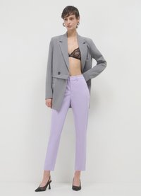 Grau gestreifter Blazer mit doppelter Knopfleiste, schwarzem Spitzen-Bralette, lavendelfarbenen Anzughosen und schwarzen spitzen Absatzschuhen. Glattes Gewebe und strukturiertes Design.