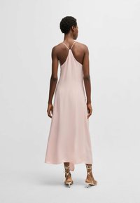 Jasnoróżowa satynowa sukienka o swobodnym fasonie, cienkich regulowanych ramiączkach i długości do połowy łydki. Gładka tekstura, minimalistyczny projekt.