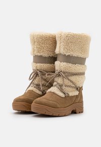 Botas impermeables de ante marrón con un puño de piel sintética color crema, cordones trenzados y suela de goma texturizada. Presenta un logo grabado en el puño.