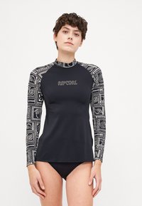 Crna dugorukašna majica za rash guard s uzorkom na rukavima u bijeloj boji, s okruglim izrezom i logom sprijeda. Nosi se preko crnih bikini gaćica.