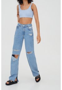 Top corto a costine blu chiaro abbinato a jeans in denim chiaro strappati con grandi strappi alle ginocchia e fessure laterali. Sandali con piattaforma neri.