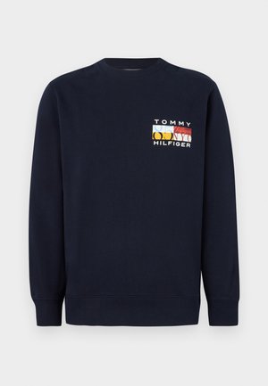 Sötétkék pulóver hosszú ujjakkal, környakú, a mellkason színes grafikai logóval. Pamut keverékből készült.