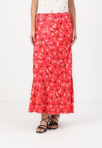 Lange roze bloemenrok met een levendig patroon van rode en crèmekleurige bloemen, voorzien van zwarte accenten en een vloeiend design. Soepele textuur.