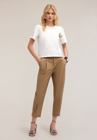 Camiseta blanca de manga corta con bolsillo y bordado de mariposa, combinada con pantalones taillados marrón claro y sandalias de tacón bloque con estampado.