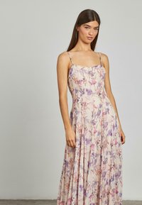 Bloemen, mouwloze maxi-jurk met een lichtroze basis, voorzien van paars en oranje bloemenpatronen, en een strakke lijfje met een vloeiende rok.