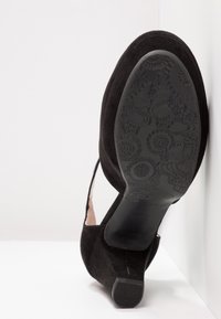 Chaussure femme en daim noir avec un talon bloc, la semelle comporte des motifs complexes de crampons floraux et géométriques.