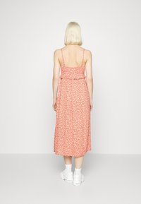 Czerwona midi sukienka w kwiaty z ramiączkami spaghetti, marszczoną górą, falbanką w talii i luźną spódnicą. Nosi ją z białymi trampkami.