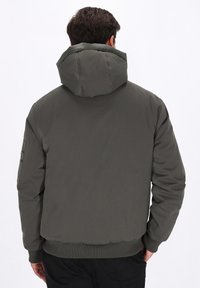 Polstret, olivengrøn jakke med en stor hætte, ribbede manchetter og kant; har minimale sømme og en glat overflade.