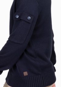 Marineblauer Strickpullover mit geripptem Saum, geknöpften Ärmeldetails und einer strukturierten Oberfläche. Verfügt über ein kleines Leder-Logo-Patch am unteren Ende.