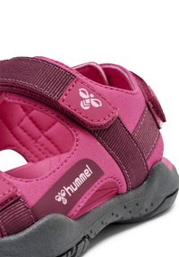 Pinke Sportsandale mit verstellbaren Riemen, verstärkter Ferse, strukturiertem Gummisohlenprofil und auffälligem Markenlogo an der Seite.