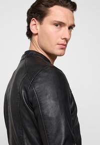 Svart läderjacka med en nära passform, försedd med en ståkrage, texturerad yta och synliga söm detaljer.